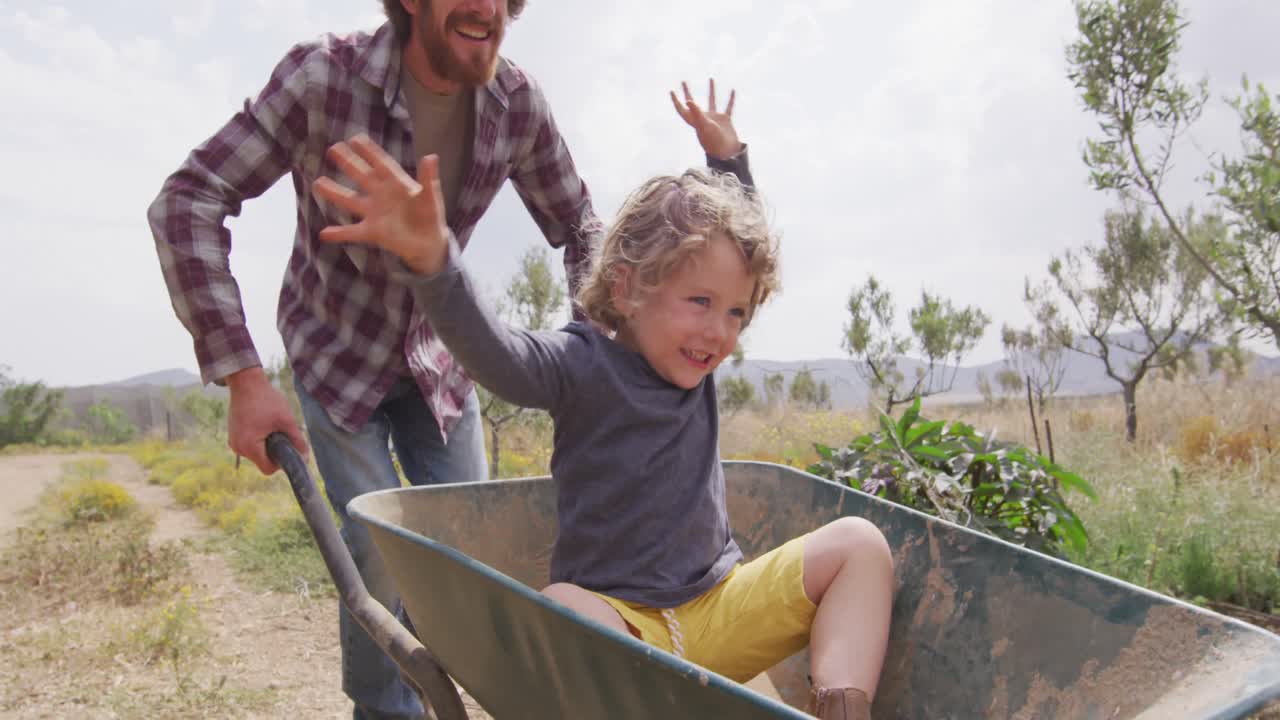 padre y hijo caucásicos felices empujando una carretilla
