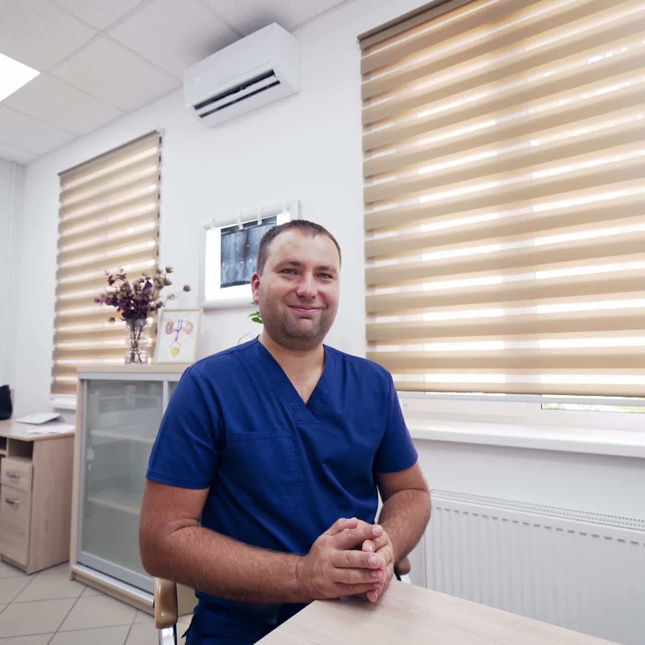 Smiling male doctor consulting online. Professional physician looking at camera and speaking calm in medical office. Telemedicine and e-health concept.