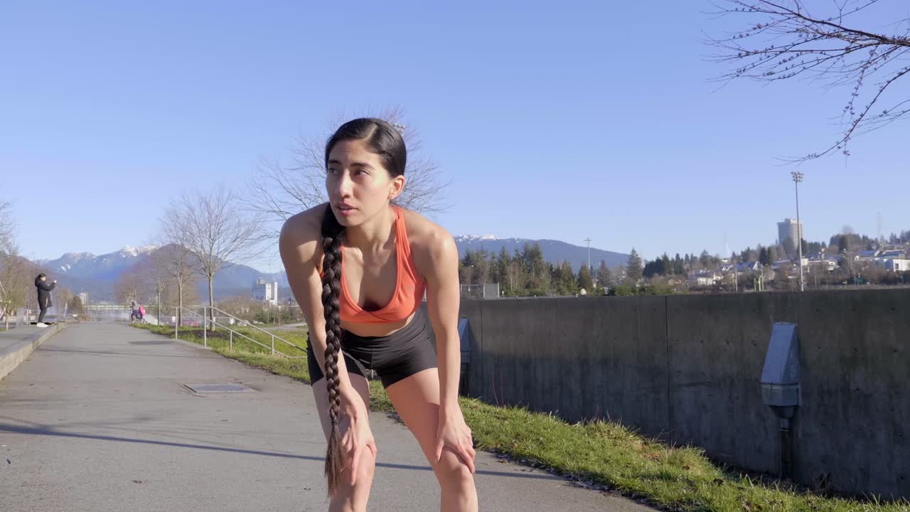 corredora latina se detiene para recuperar el aliento con las manos en las rodillas en sostén deportivo naranja