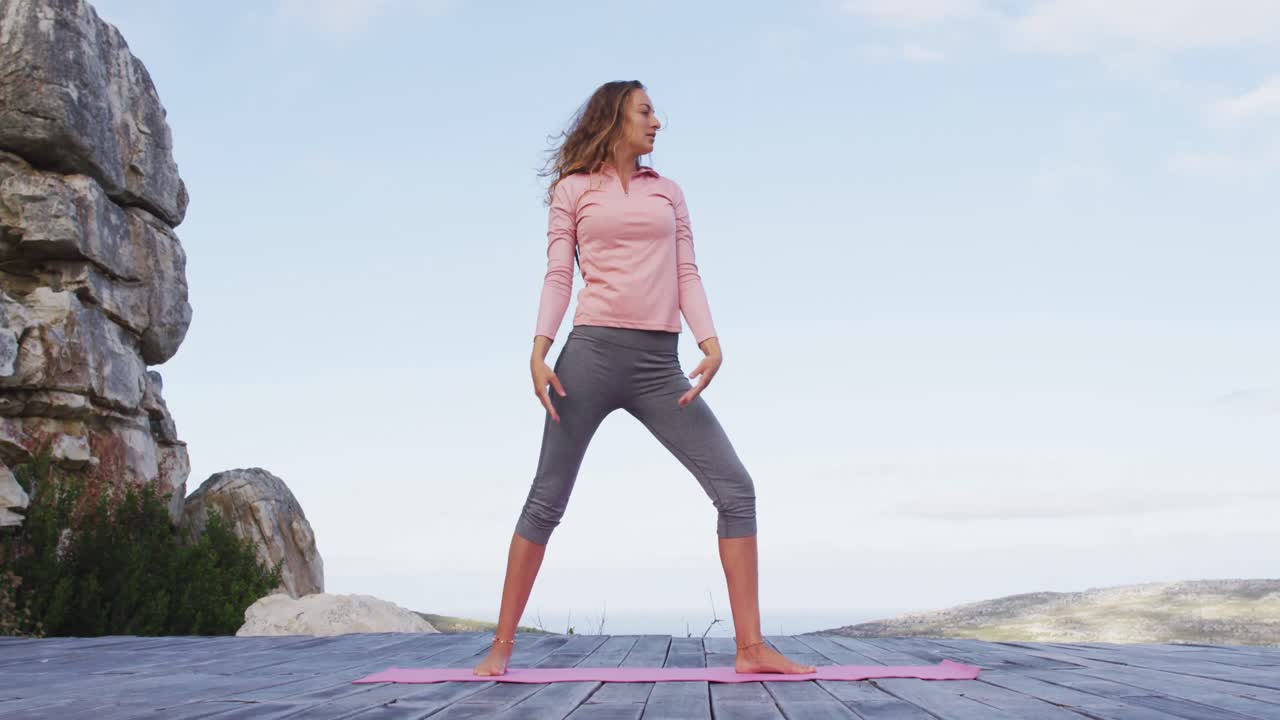mujer caucásica practicando yoga al aire libre de pie en la cubierta estirándose en un entorno montañoso rural