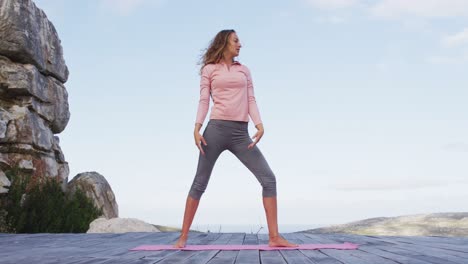 caucasian woman practicing yoga outdoors standing on deck stretching in rural mountainside setting