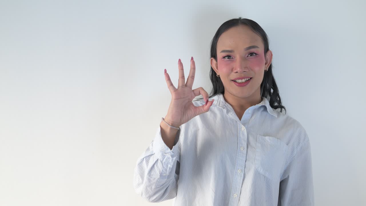 Thai transgender person making Ok sign gesture against white background indoors