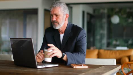 Businessman-having-coffee-while-using-laptop-on-table-4k