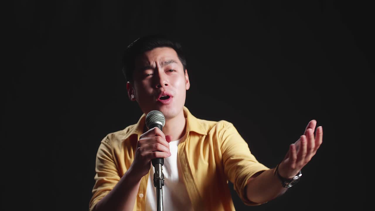 Asian Man Singer Singing Into Microphone On Black Background