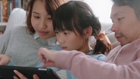 happy asian family using tablet computer little girl watching entertainment with parents playing game on touchscreen device browsing online relaxing on sofa together at home 4k footage