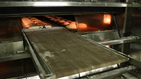 a baker manually pulling the deck oven loader, moving the raw bread dough into the oven - bread making in a bakery - slow motion