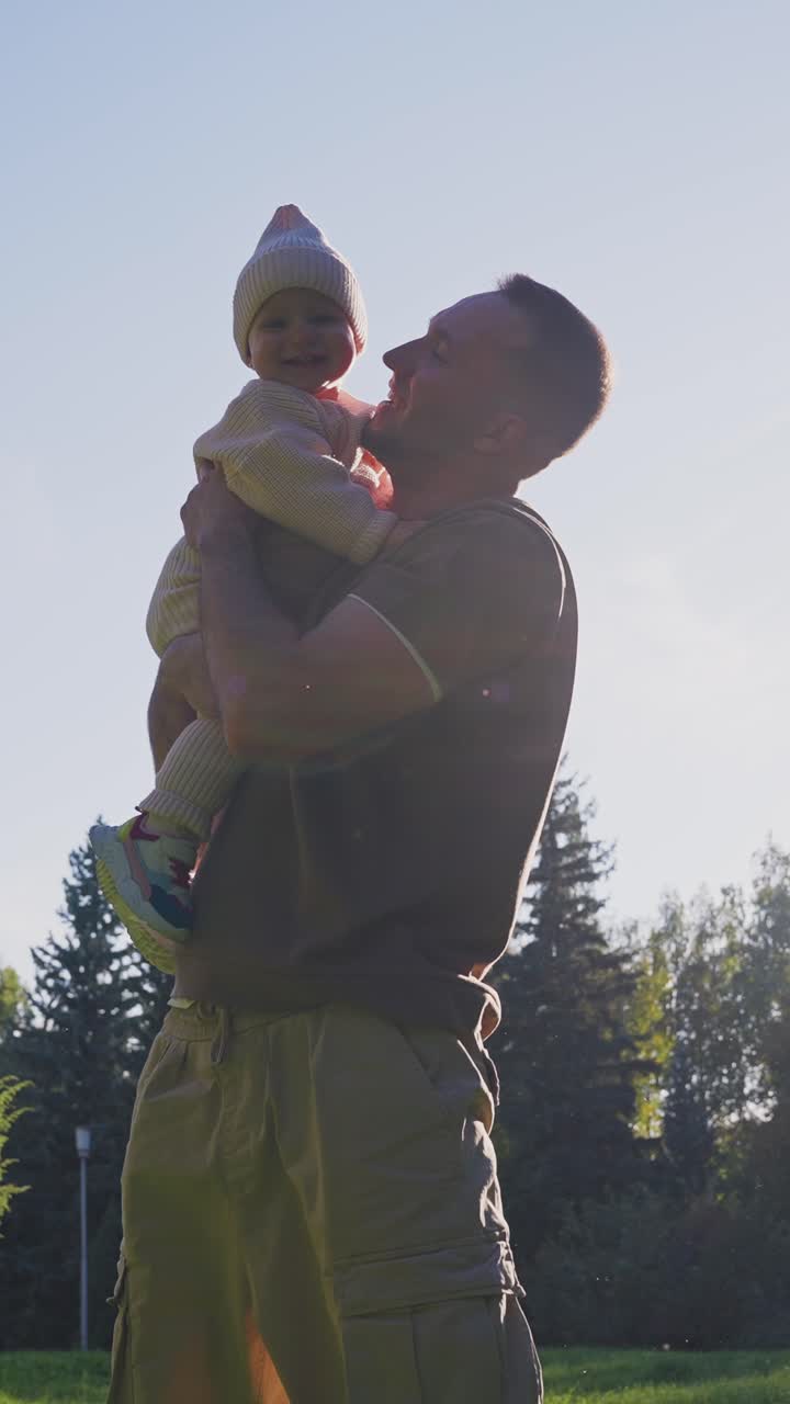 Padre feliz ayuda a su bebé a dar sus primeros pasos en un parque soleado