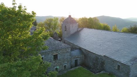 Vertical drone takeoff with backlit view of Santa María la Real bell tower at sunset in O Cebreiro. Spiritual and emotional atmosphere on the Camino de Santiago, Galicia, Spain.