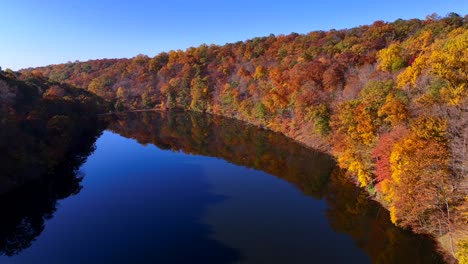 an aerial view of a reflective lake on a sunny day with colorful autumn trees on both sides