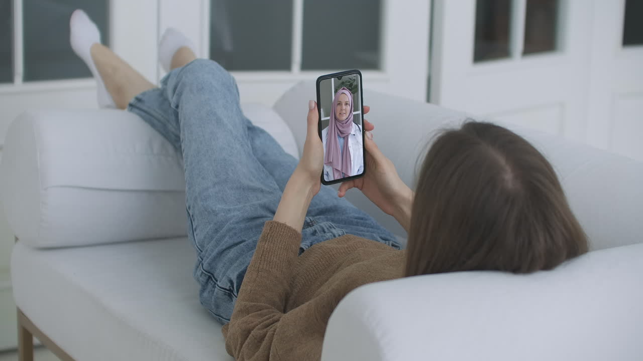 mujer usando una aplicación médica en un teléfono inteligente consultando con un médico musulmán con pañuelo en la cabeza a través de videoconferencia. mujer usando chat en línea para hablar con un terapeuta familiar y chequear posibles síntomas durante