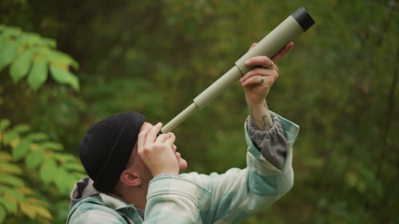 Scout examines tools, Autumntoned outdoor setting with gear and reconnaissance activities, Male survivalist in green woods checks distant landmark using handmade spyglass and compass