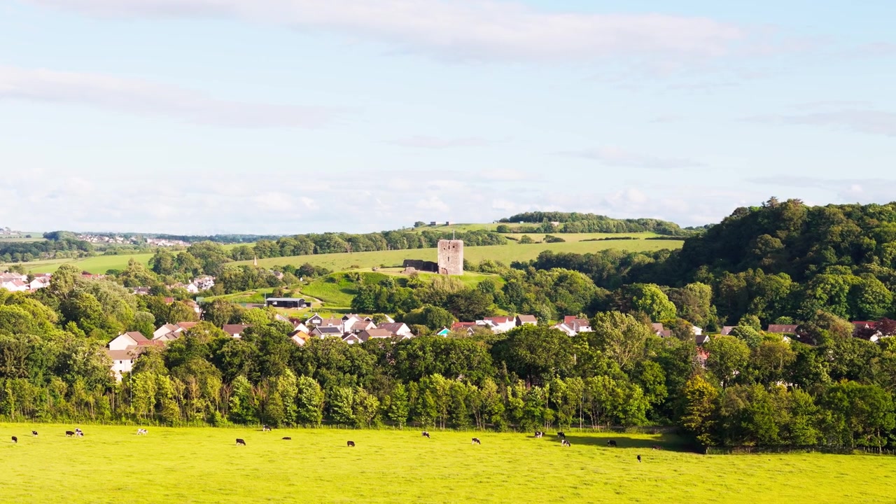 Vila de Dundonald e as ruínas do castelo histórico em Ayrshire, Escócia, rodeadas por terras agrícolas, bosques e paisagens onduladas, vista aérea cinematográfica