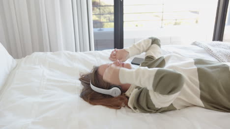 relaxing on bed, young woman listening to music with headphones