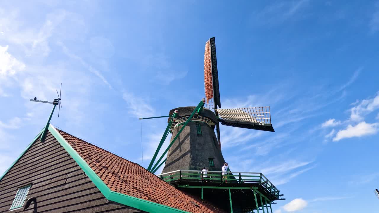 Historic windmill blades turning smoothly, bright daylight, vibrant sky, static camera, Dutch countryside