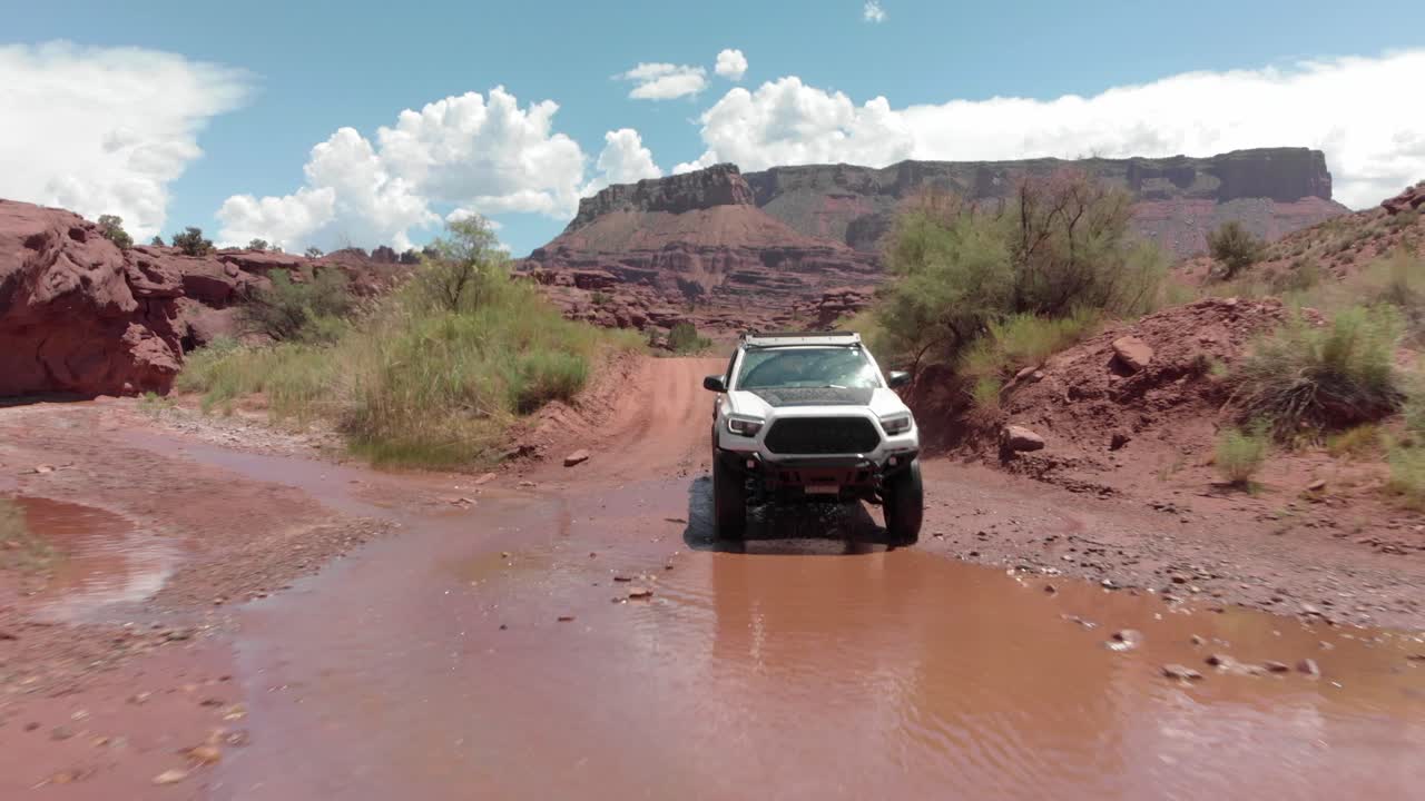 Rugged white truck splashes through shallow Utah desert river crossing