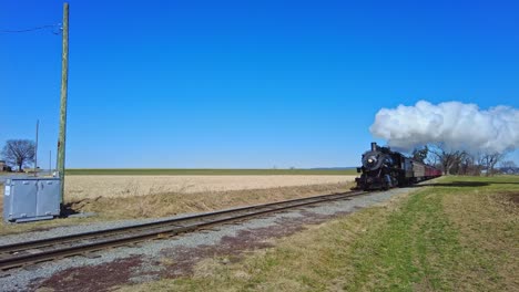 un tren de pasajeros de vapor que se acerca soplando humo y vapor en un día soleado