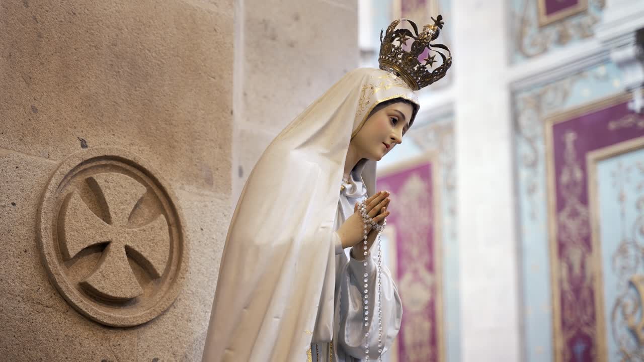 Statua della Vergine Maria con abito bianco e rosario tra le mani, all'interno di una chiesa