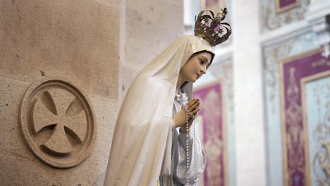 statue of virgin mary with white dress and rosary in hands, inside church