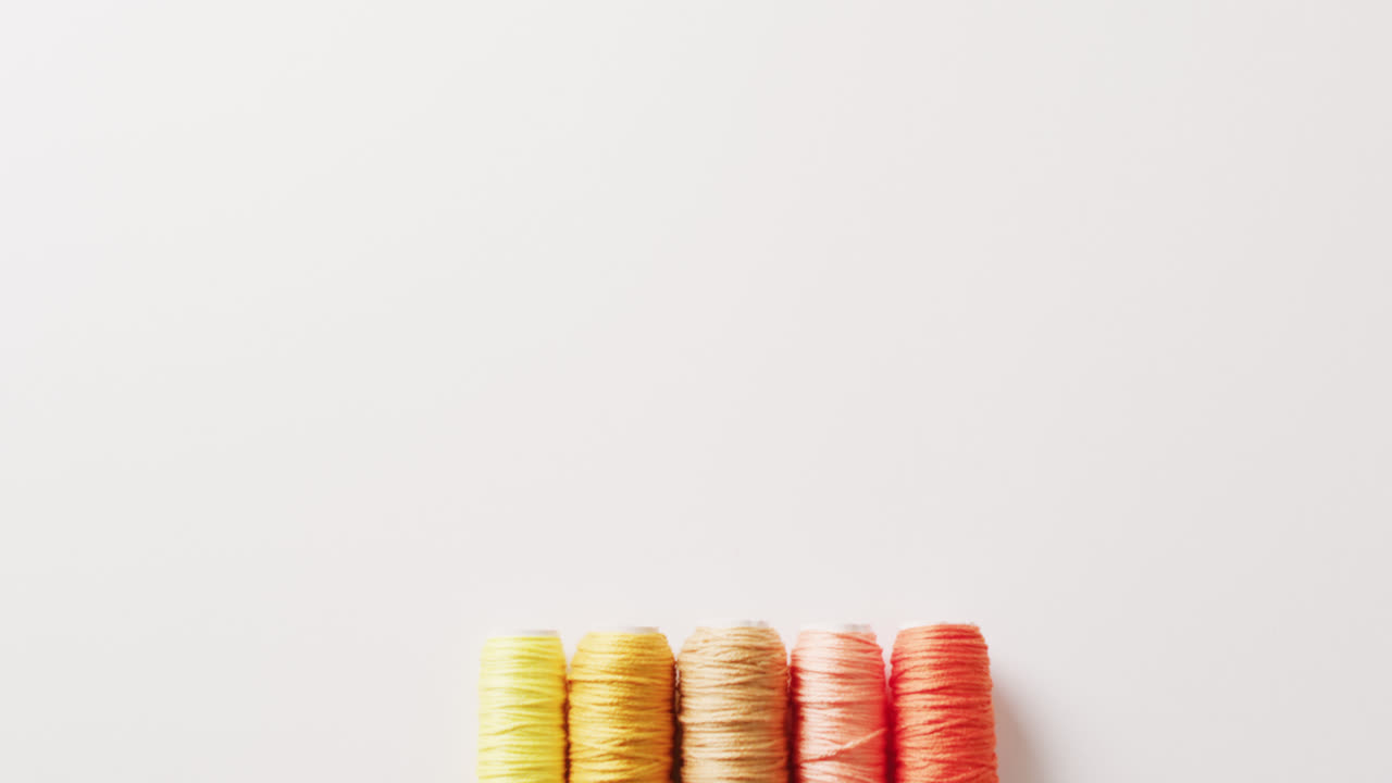 vídeo de cinco carretes de hilos de bordado de amarillo a naranja sobre fondo blanco con espacio para copiar