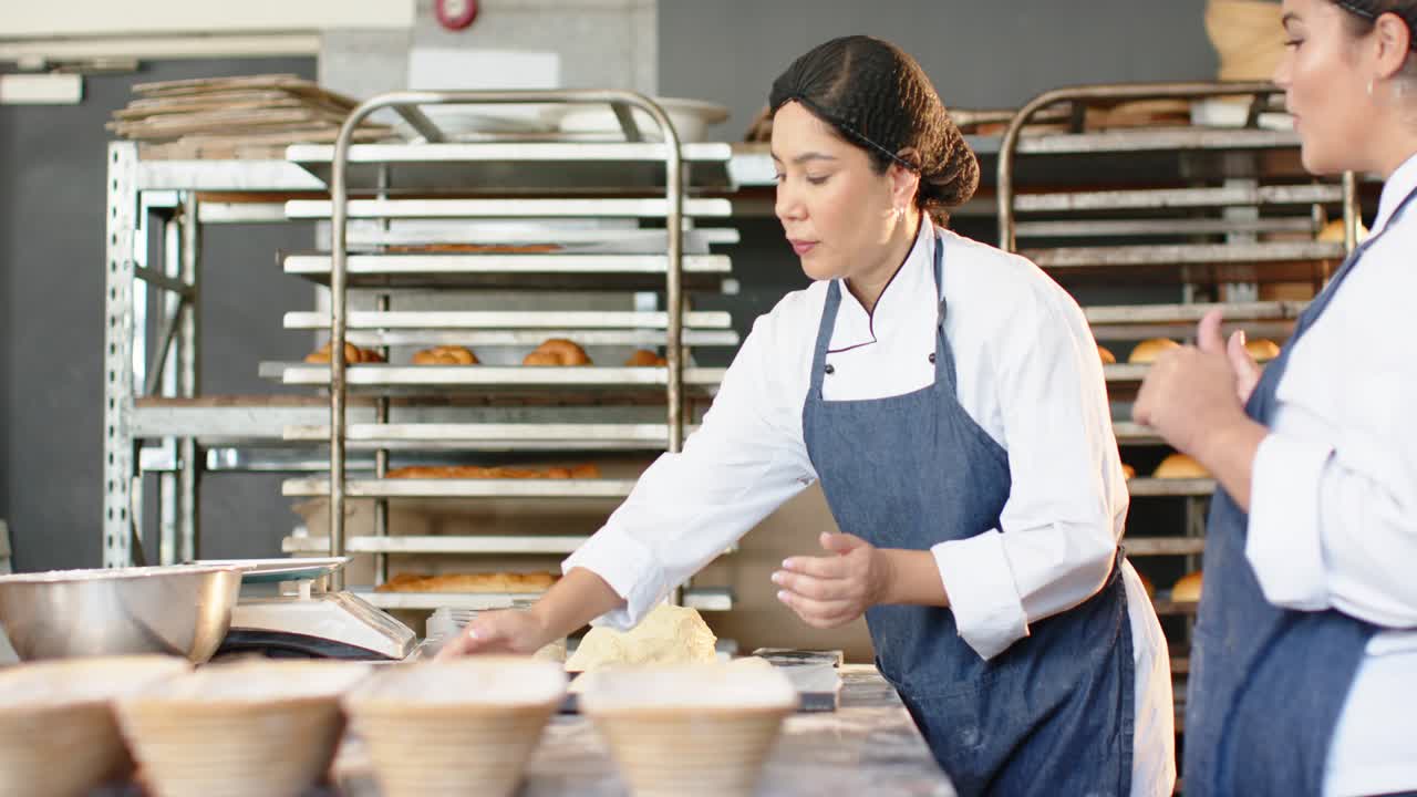 Ulike kvinnelige bakere former og veier deig med vekt i et bakeri, mens en assistent kommer inn for baking.