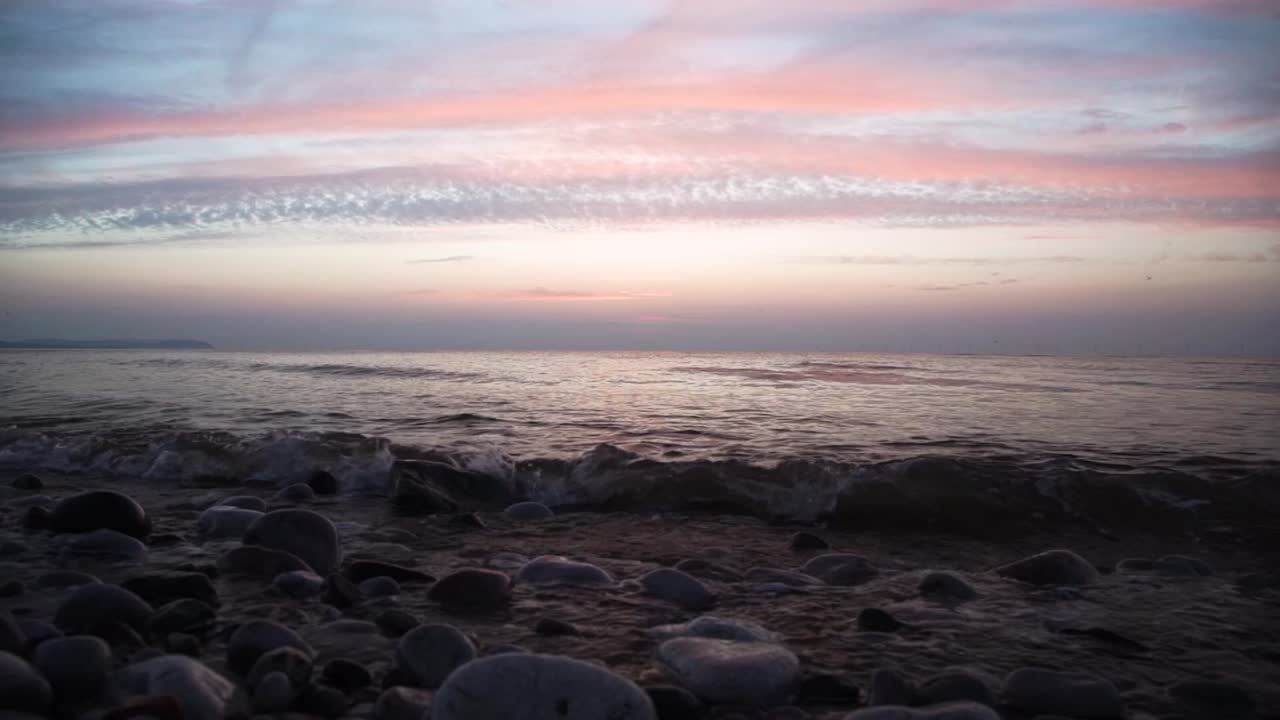 calm small sea waves at colorful sunset sky on round rock beach