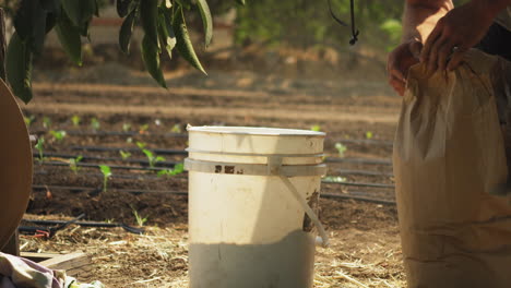 Close-up-of-white-bucket-on-ground-where-powdered-fertilizer-is-poured-from-a-sack