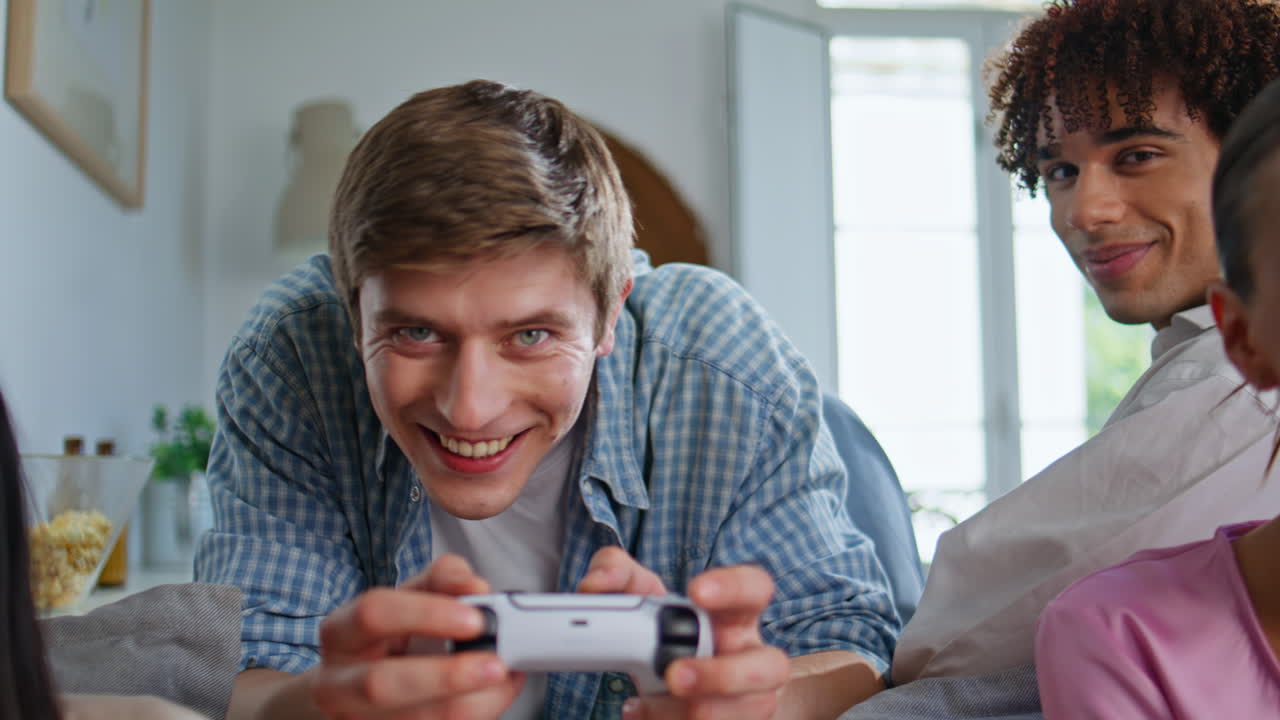 Adolescente concentrato che si diverte con i videogame in un appartamento, primo piano. Festa tra amici diversi