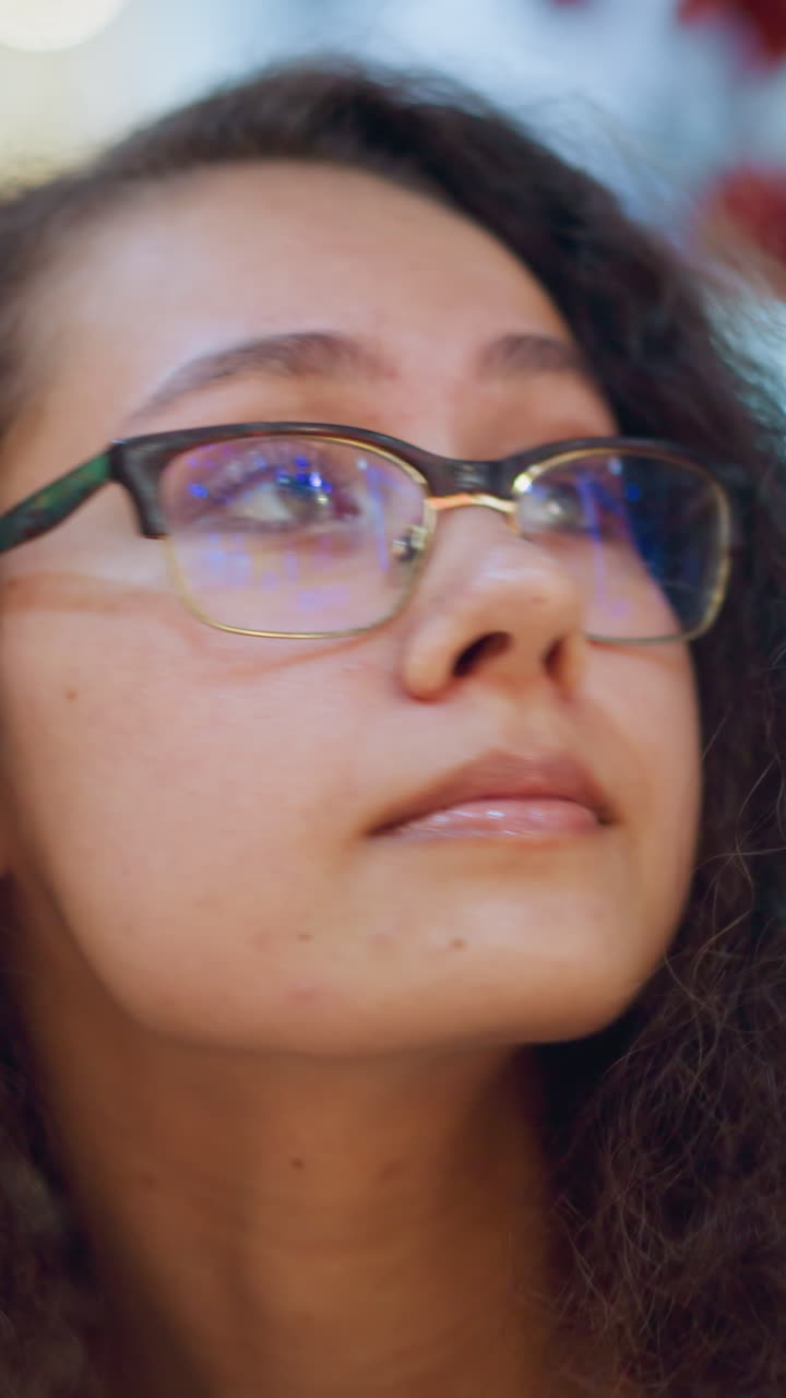 mujer con cabello rizado y gafas en un centro comercial bien iluminado, mirando a su alrededor con una expresión reflexiva, el fondo muestra luces bokeh suaves, creando un ambiente interior vibrante y cálido
