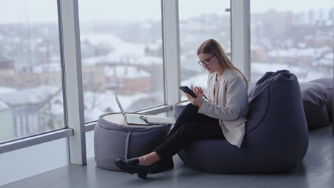 young woman employee sitting in a bean bag armchair and looks at her phone. nice working space in modern office.