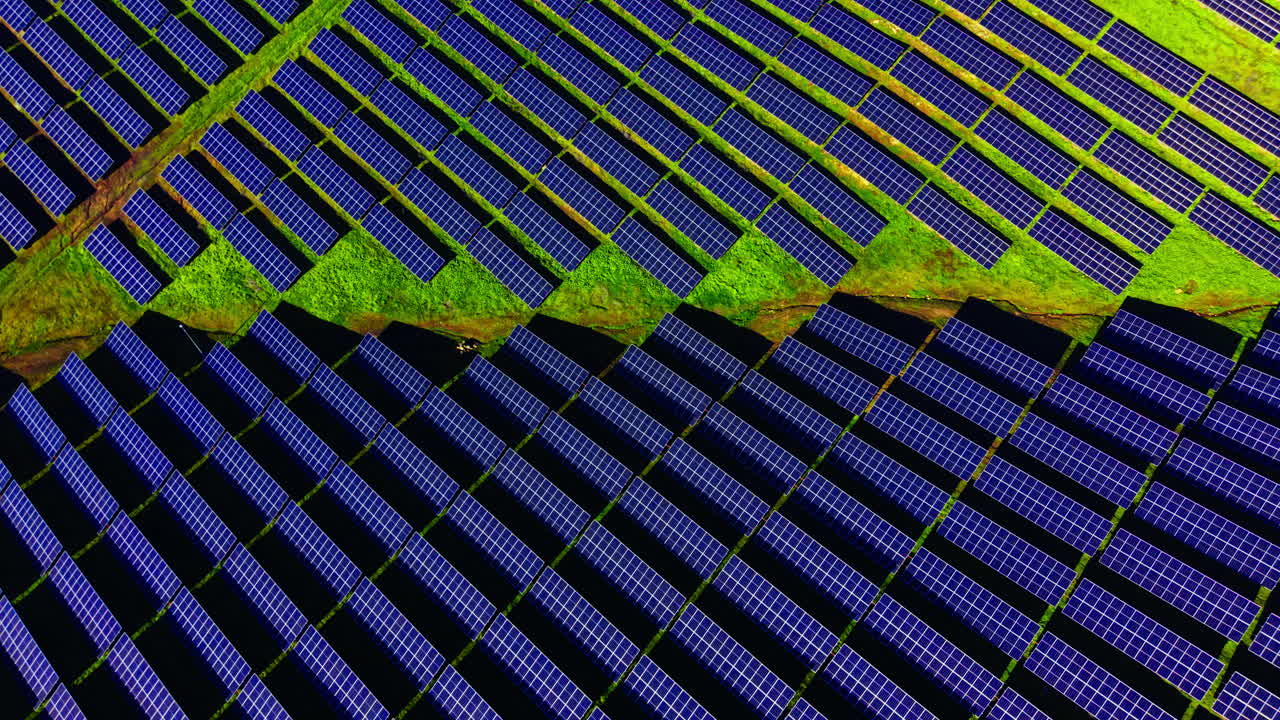 Vista dall'alto ad angolo elevato di pannelli fotovoltaici blu disposti in motivi geometrici su erba verde brillante