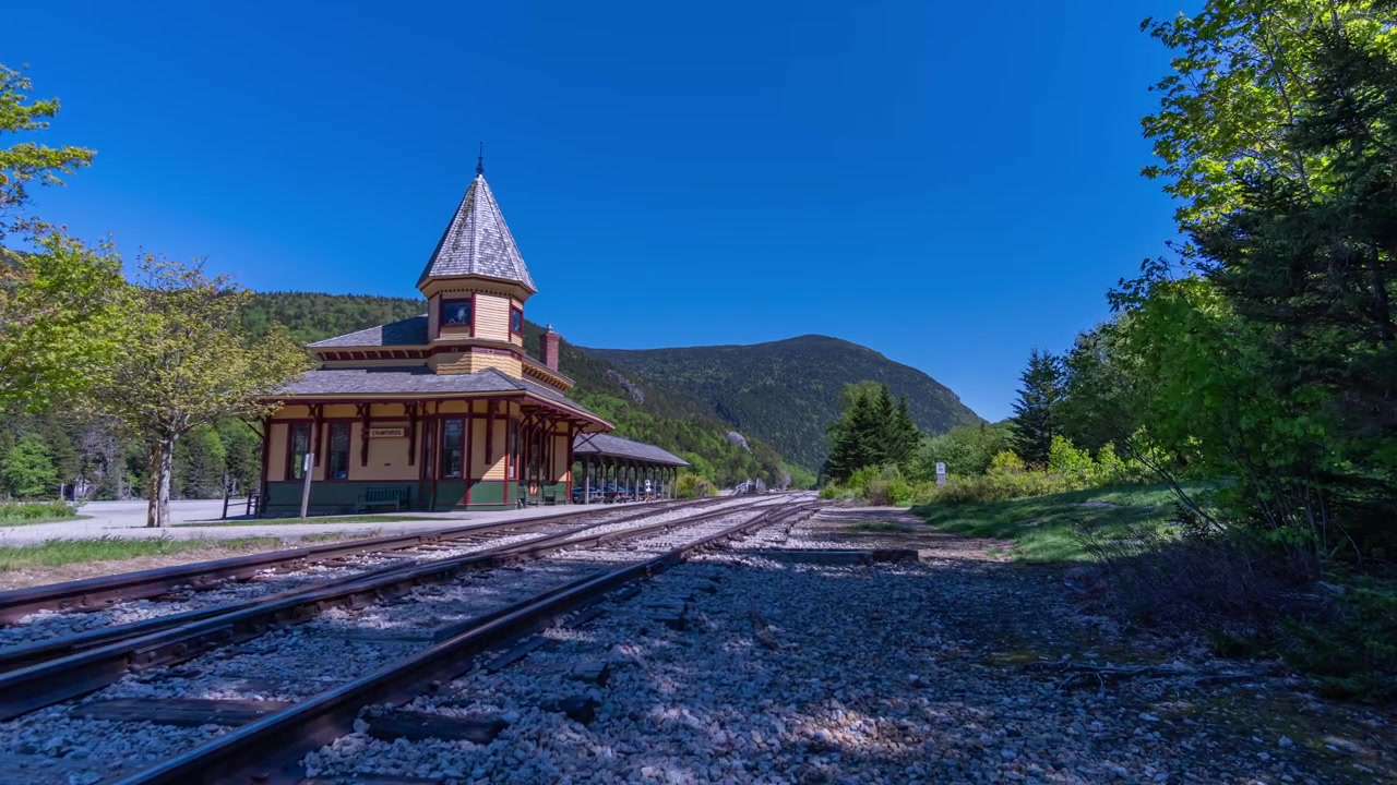 Time-lapse-kuvaus Crawford Notch Depotista tyhjien rautatiekiskojen vieressä kirkkaan sinisen taivaan alla White Mountainin kansallispuistossa, Lincolnissa, New Hampshiressä, Yhdysvalloissa.
