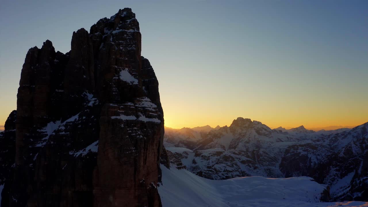 Aerial reveal of sun at Tre Cime di Lavaredo snowy mountain in Italian Dolomite at sunset