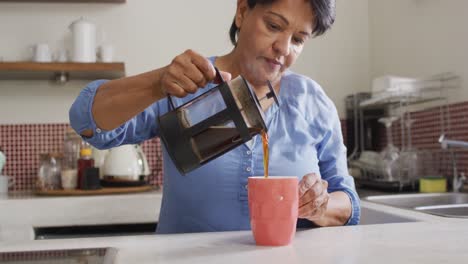 Asian-senior-woman-pouring-coffee-in-her-cup-in-the-kitchen-at-home