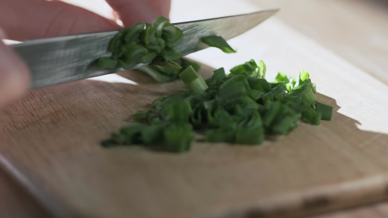 clip en bucle de una mujer cortando cebolla verde en la cocina con un cuchillo, vista de cerca