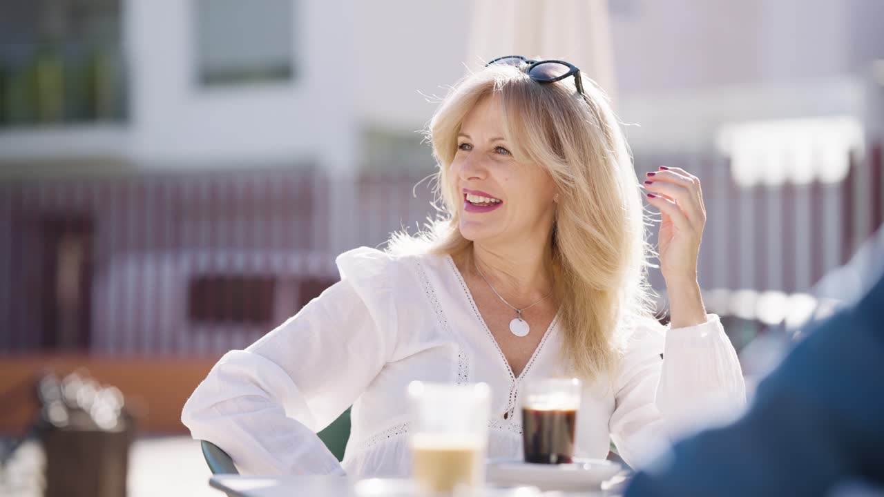 Donna allegra che si gode un caffè e chiacchiera in un bar all'aperto soleggiato