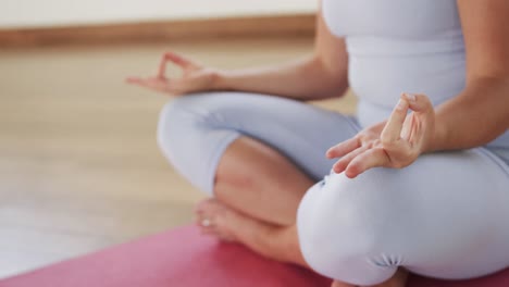 midsection of caucasian woman practicing yoga meditation in gym, slow motion