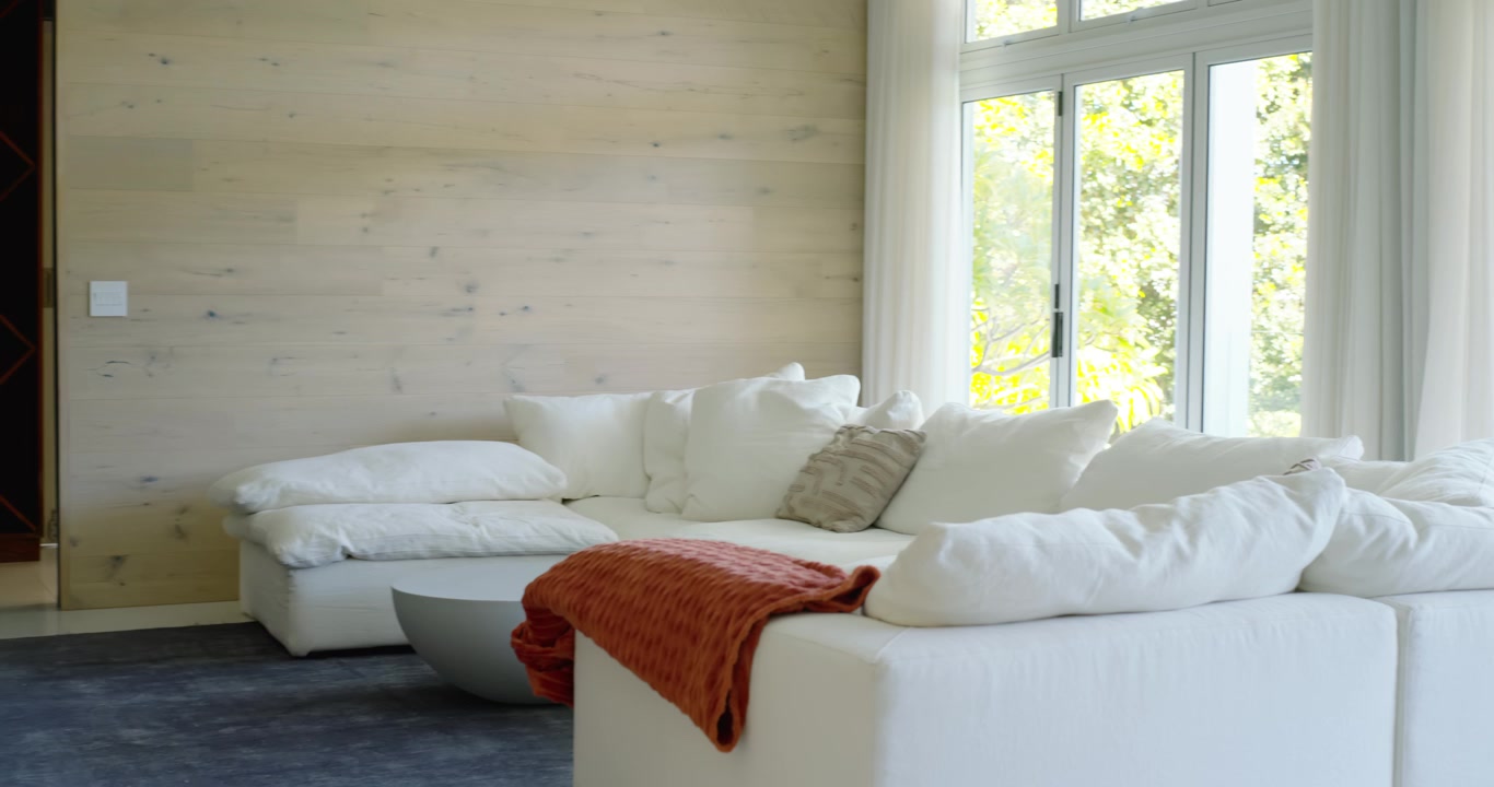 Camera is starting pan right, revealing sofa, rust throw and window to show living room layout