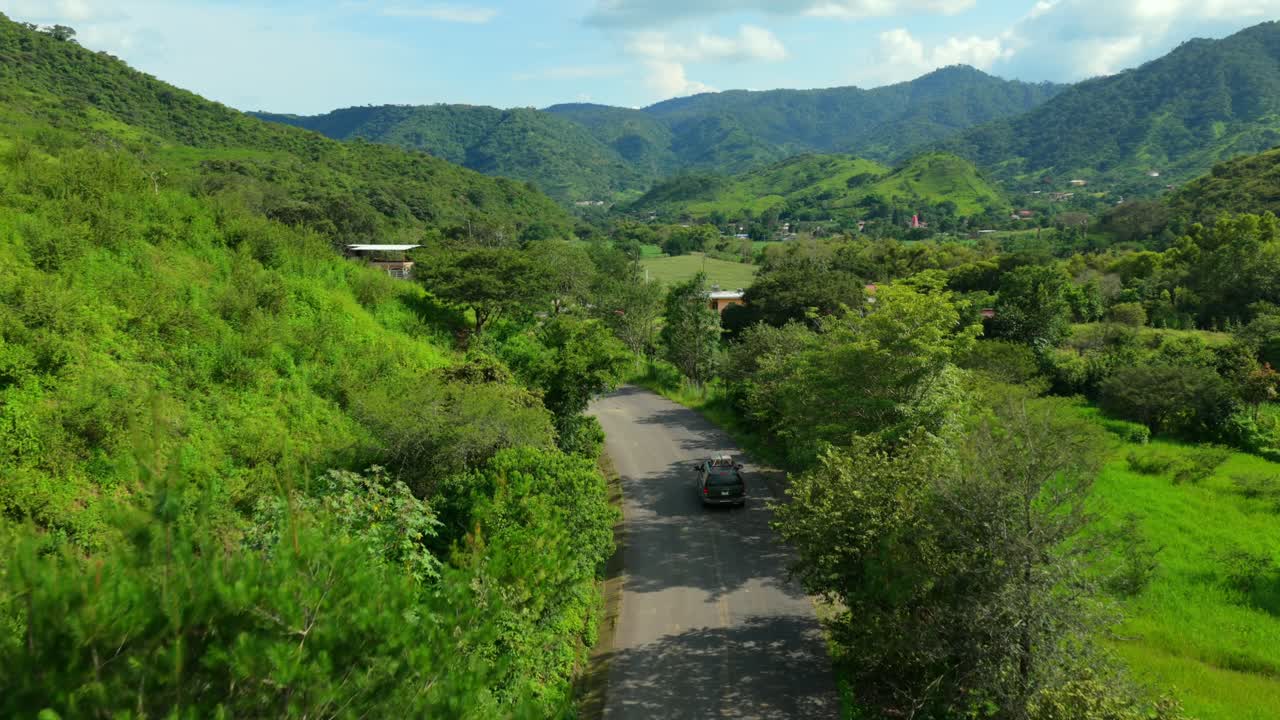 Aerial view of 4x4 SUV driving on narrow rural road through green hills and farmland in Jalisco, Mexico
