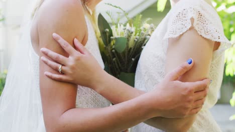 pareja de mujeres diversas sosteniendo un ramo de flores y abrazándose en el jardín