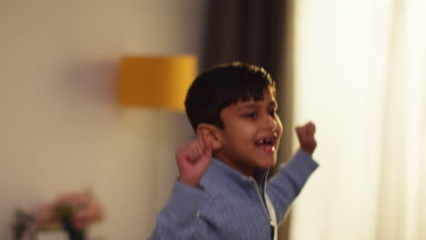 disruptive young boy behaving badly at home jumping on sofa in lounge