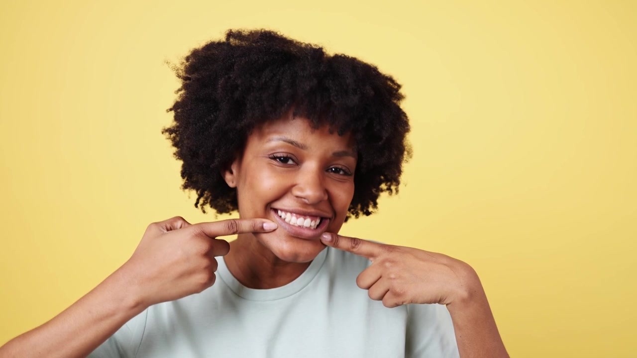 Donna afroamericana felice che sorride e indica i suoi denti sani.