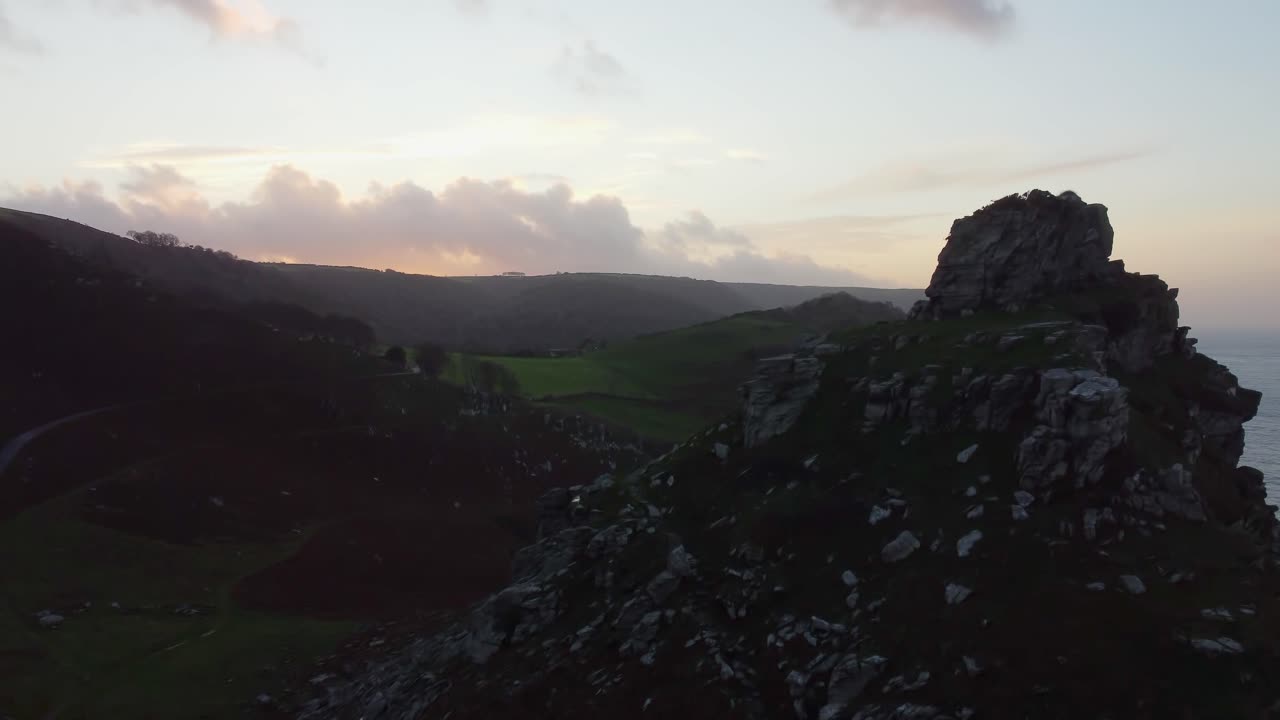 dron aéreo en ascenso con la luz del atardecer más allá de la cima del acantilado en el valle de las rocas exmoor uk 4k