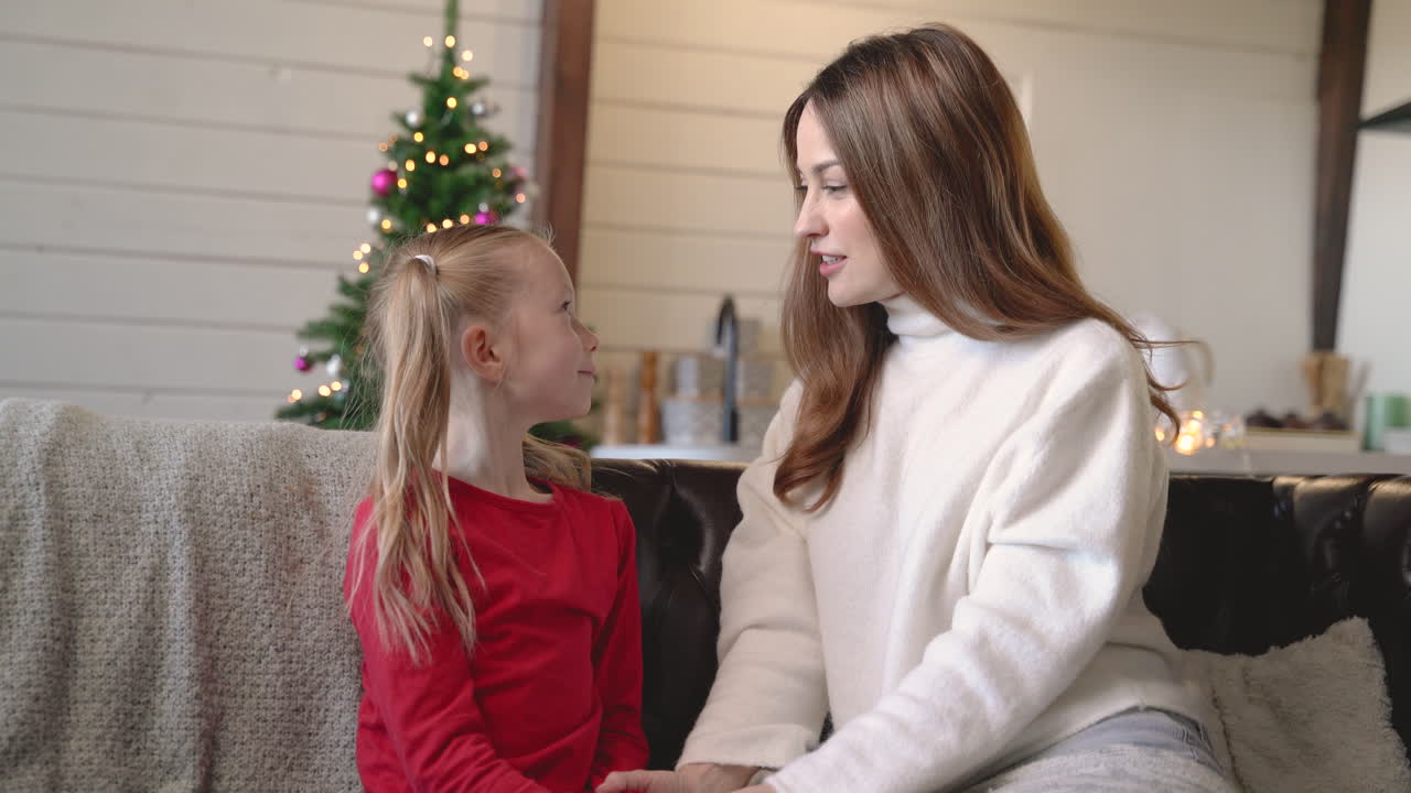 Mor og datter taler sammen, siddende på sofaen i stuen med julepynt
