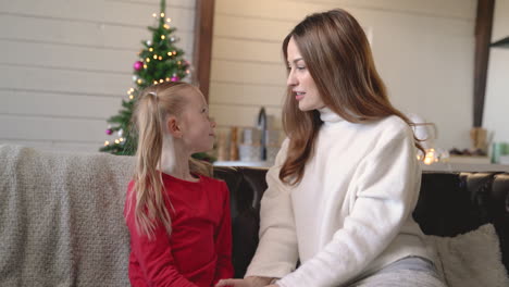 mother and daughter talking sitting on the sofa in living room with christmas decorations