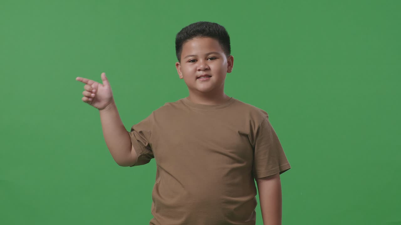 녹색 스크린에 서 있는 동안 을 가리키는 미소로 아시아 소년