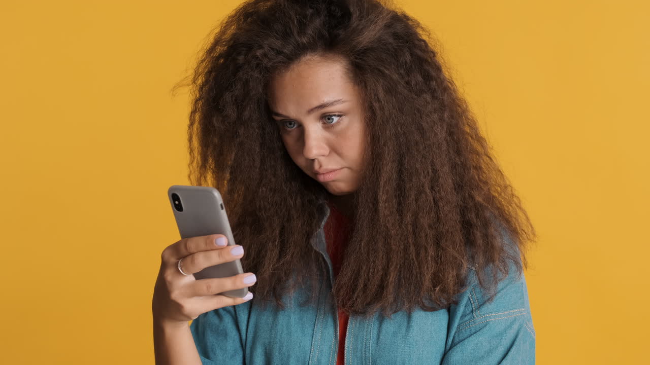 Bored Caucasian curly haired woman using smartphone.