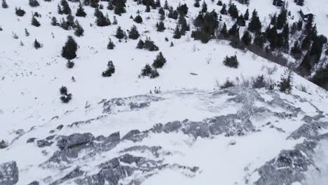 4K-aerial-tilt-up-reveal-of-Norwegian-snow-mountain-winter-landscape-with-rocks-in-the-foreground-on-a-cloudy-moody-day