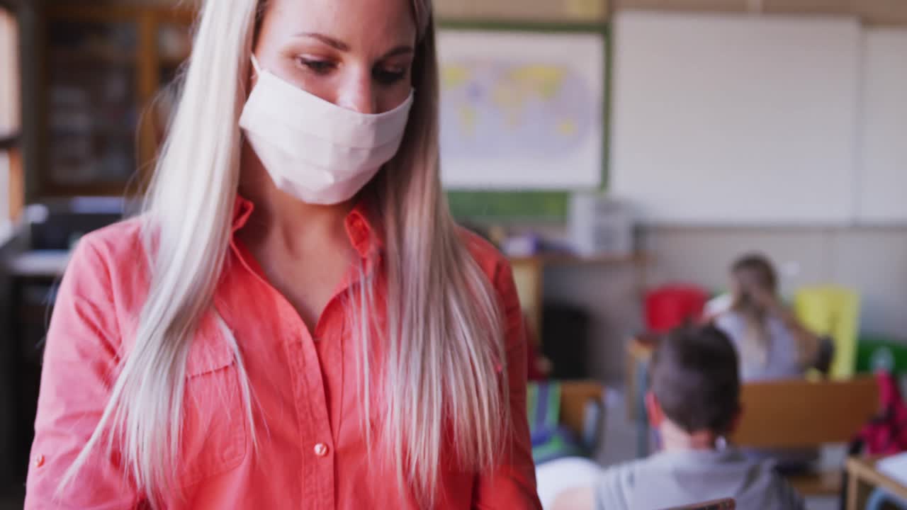 학교에서 디지털 태블릿을 사용하여 얼굴 마스크를 쓰고 있는 여성 교사