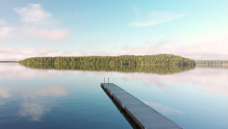 crane move up above a wooden pier at a calm serene lake watching a small island far away