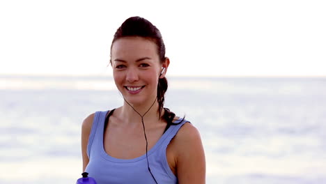 mujer bebiendo agua en la playa y sonriendo a la cámara